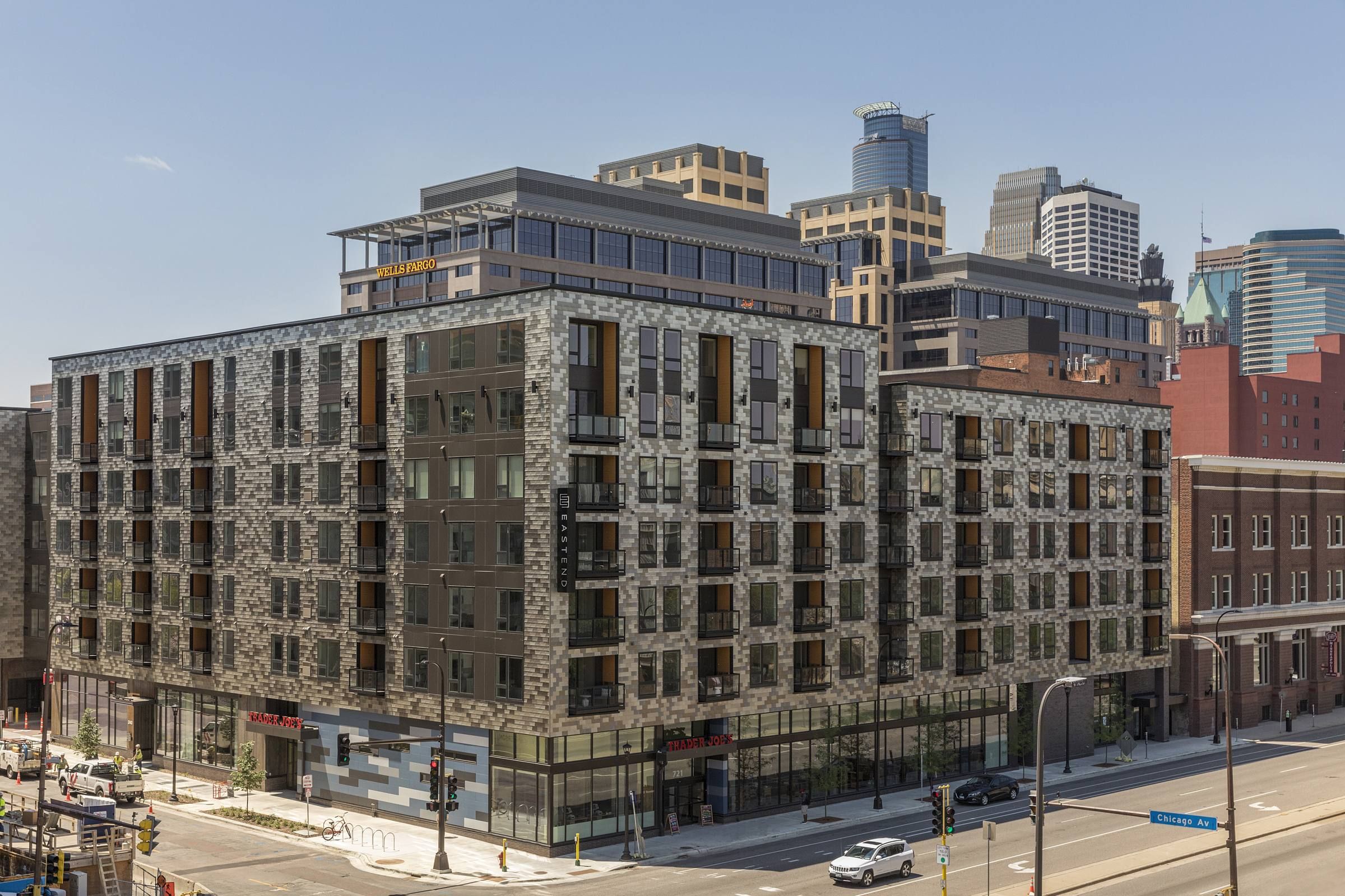 Modern multi-story building with stone facade and large windows, located in an urban setting with nearby skyscrapers and retail spaces.