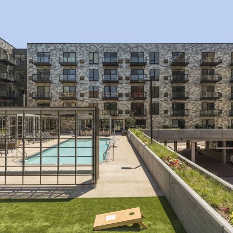 Modern apartment complex with a pool area, surrounded by greenery and sleek architecture, featuring balconies and lounging spaces.