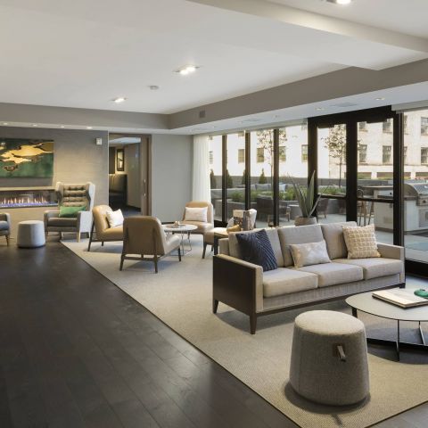 Modern lounge area featuring stylish chairs, a sofa, and a cozy fireplace, with large windows overlooking an outdoor space.
