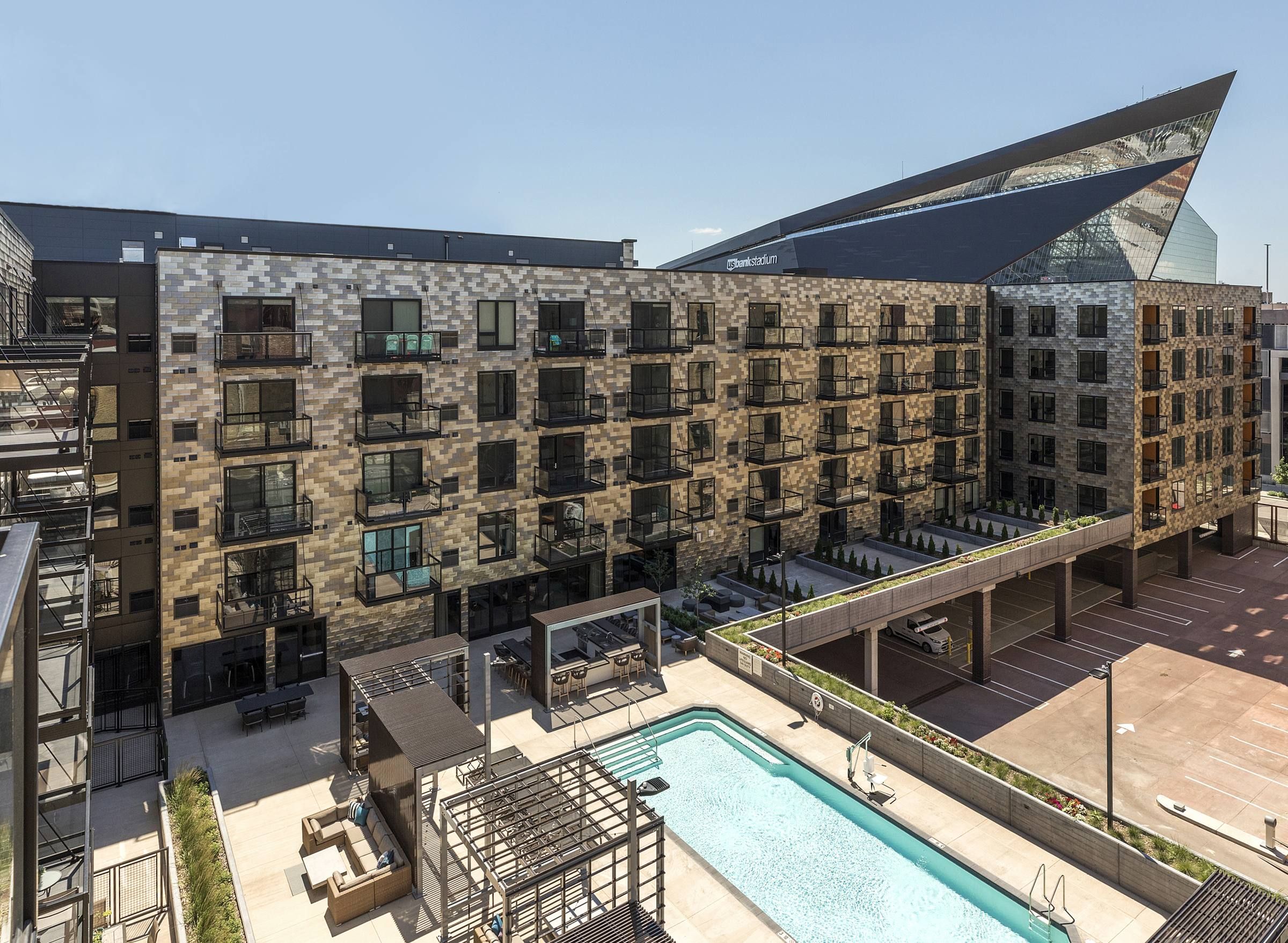 Modern apartment building with balconies, pool area, and outdoor spaces, against a clear blue sky.